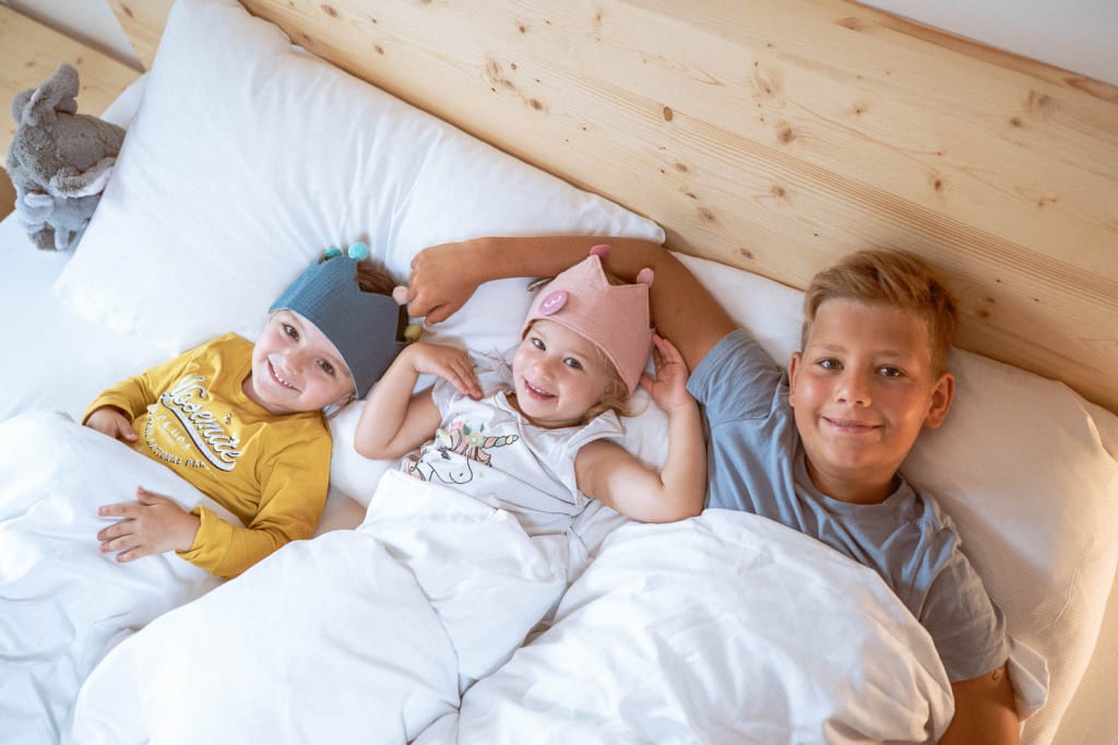 drei lachende Kinder liegen gemütlich im Bett