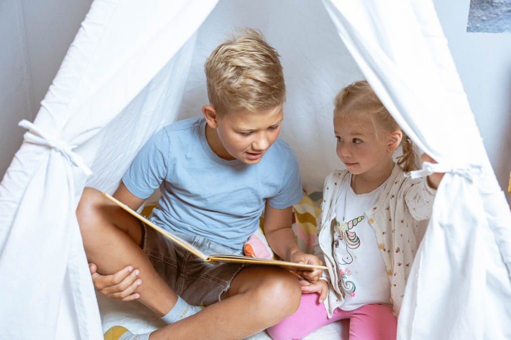 Junge liest Mädchen in einem Spielzelt aus einem Buch vor