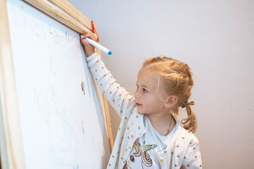kleines Mädchen schreibt auf einer Kindertafel