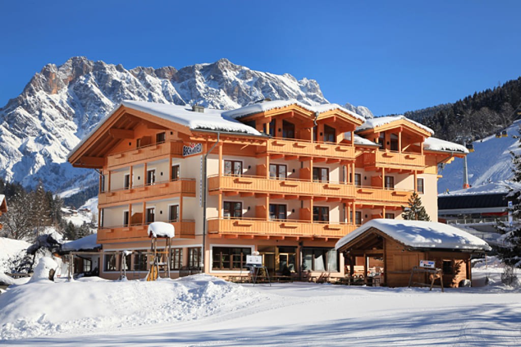 verschneites Hotel Bachschmied in Maria Alm vor blauem Himmel und Bergkulisse